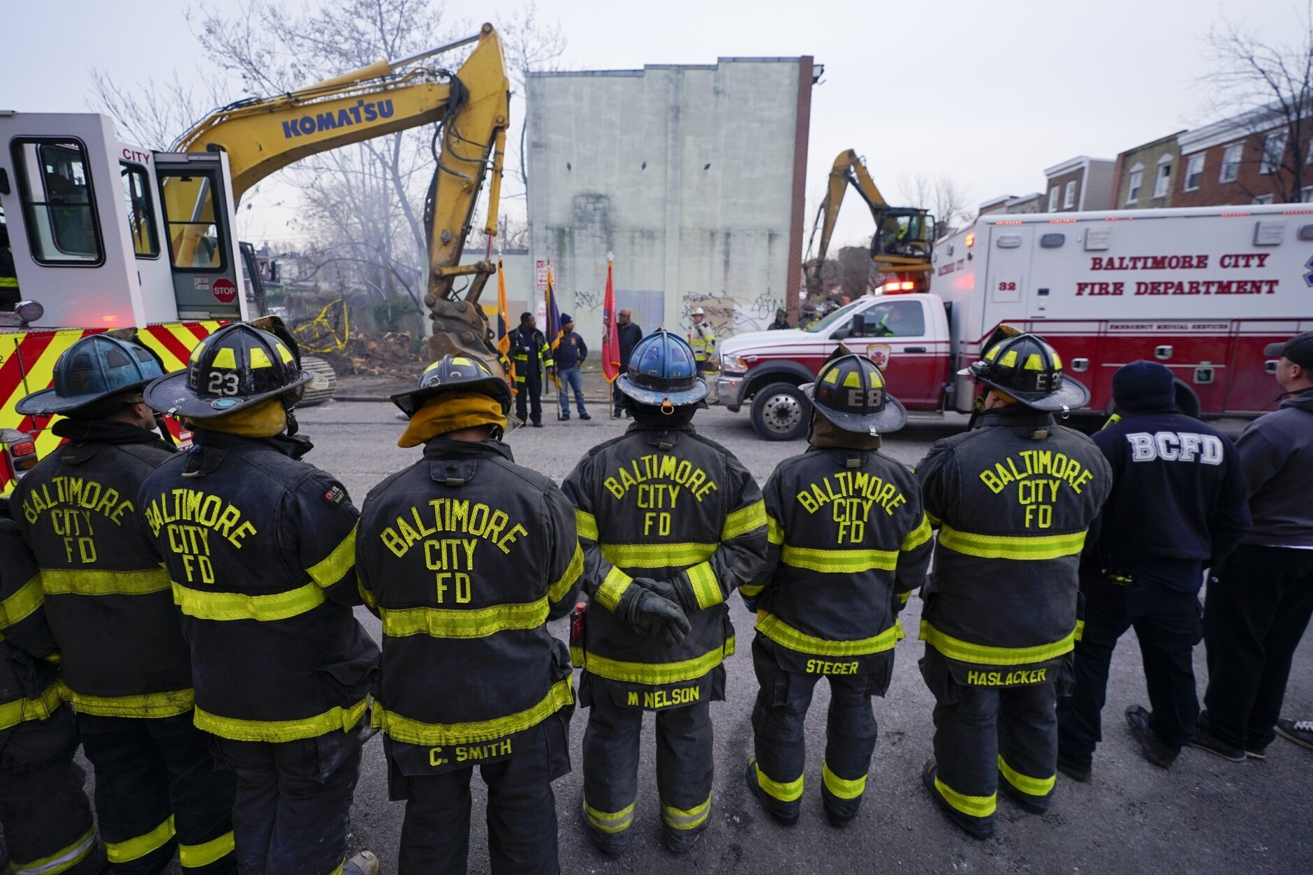 Firefighters stand in a line near an ambulance after a firefighter who died while battling a two-alarm fire in a vacant row home was pulled from the collapsed building, Monday, Jan. 24, 2022, in Baltimore. Officials said several firefighters died during the blaze. (AP Photo/Julio Cortez)