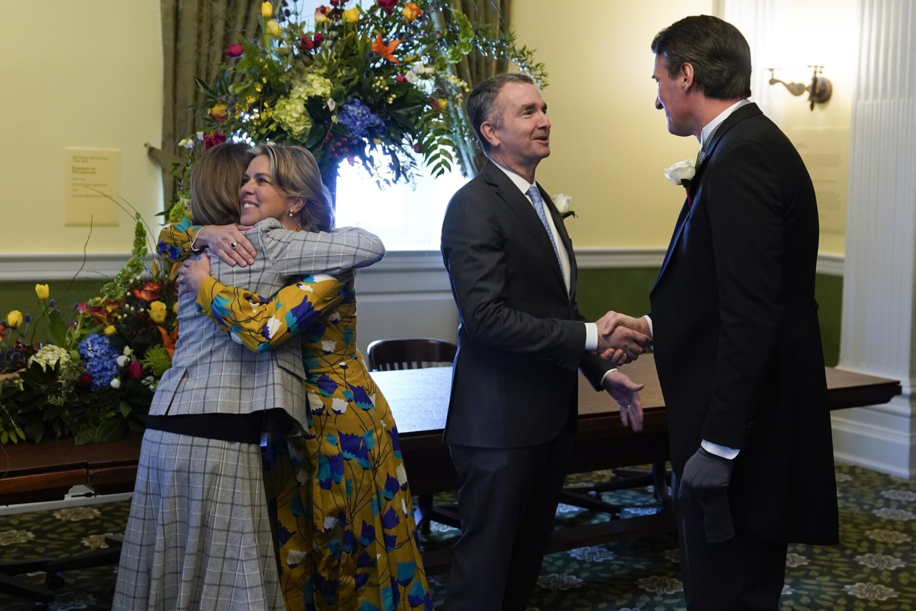 Virginia Gov. Ralph Northam greets Gov. elect Glenn Youngkin as Pam Northam, left, empraces Suzanne Youngkin before an inauguration ceremony, Saturday, Jan. 15, 2022, in Richmond, Va. (AP Photo/Steve Helber)