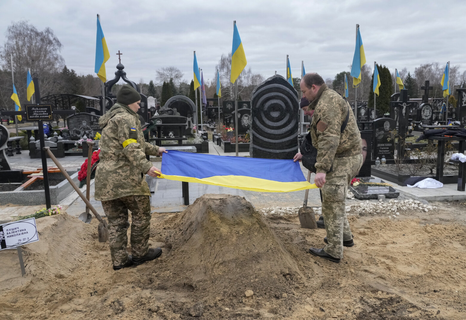 Ukrainian paramedics cover with the National flag the grave of their colleague Valentyna Pushych, killed by Russian troops, in a cemetery in Kyiv, Ukraine, Saturday, March 5, 2022. (AP Photo/Efrem Lukatsky)