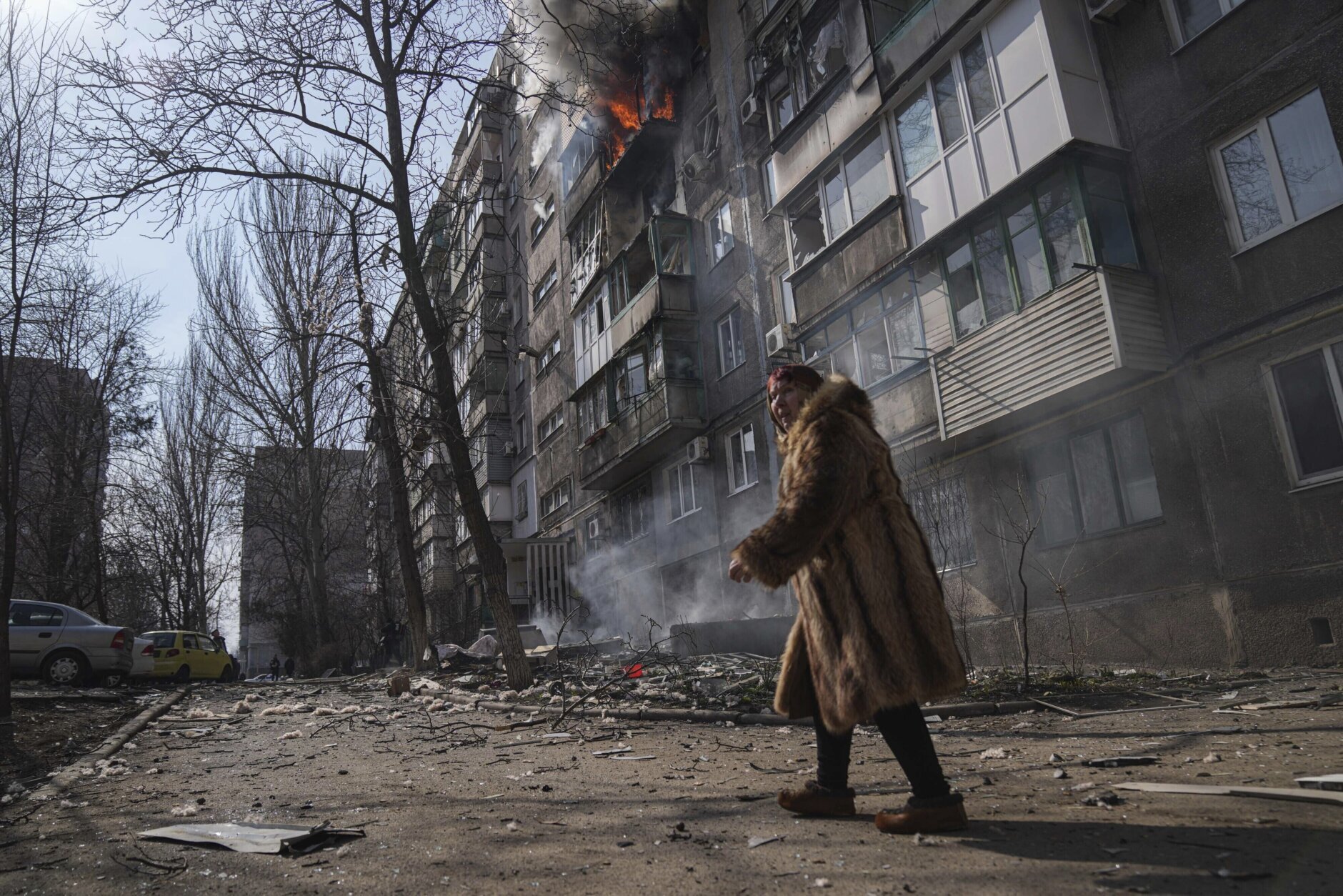 <p>A woman walks past a burning apartment building after shelling in Mariupol, Ukraine, Sunday, March 13, 2022.</p>

