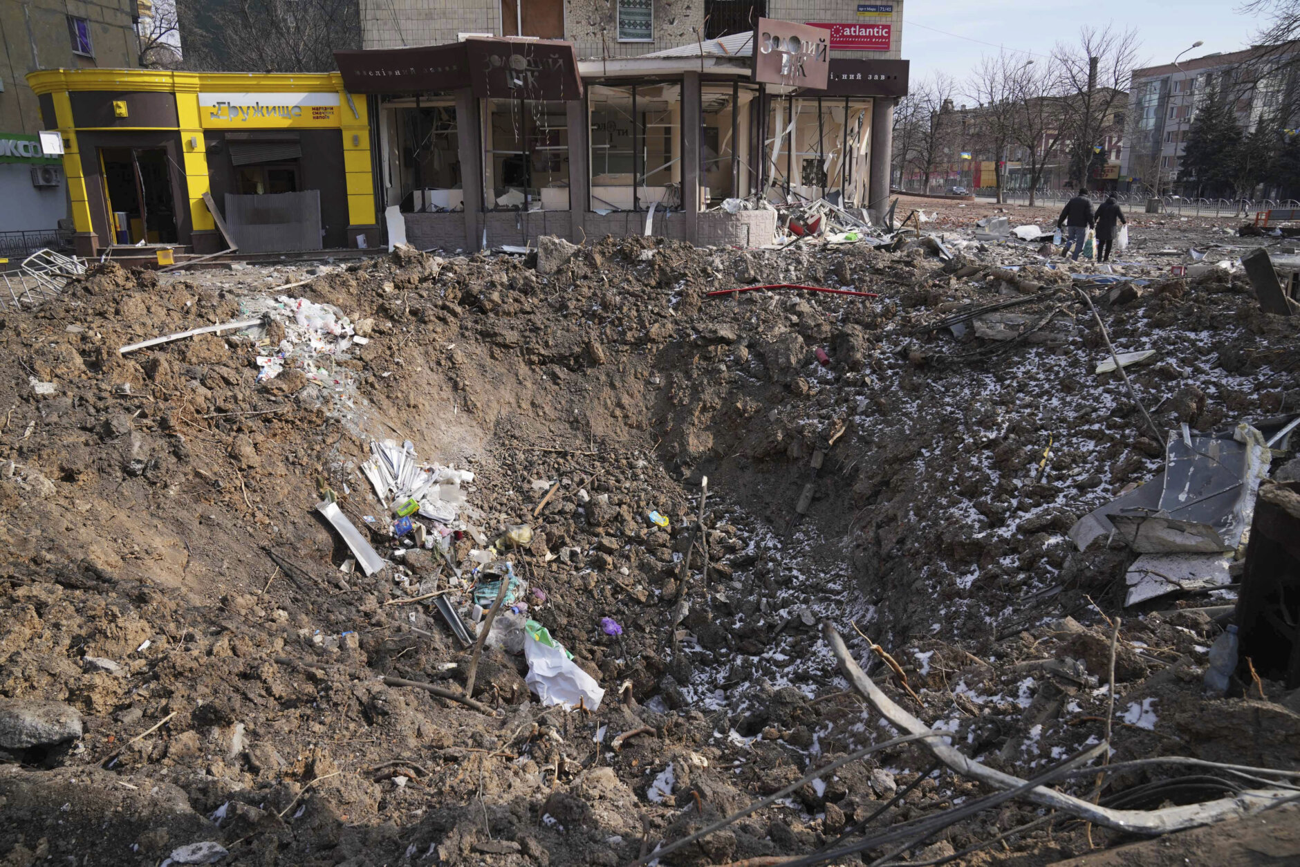 <p>People walk past a crater from the explosion in Mira Avenue (Avenue of Peace) in Mariupol, Ukraine, Sunday, March 13, 2022. The surrounded southern city of Mariupol, where the war has produced some of the greatest human suffering, remained cut off despite earlier talks on creating aid or evacuation convoys.</p>
