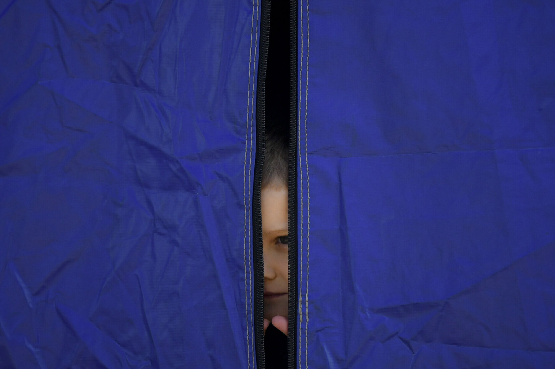 <p>A refugee fleeing the war from neighbouring Ukraine peers from a tent after crossing the border, at the Romanian-Ukrainian border, in Siret, Romania, Monday, March 14, 2022.</p>
