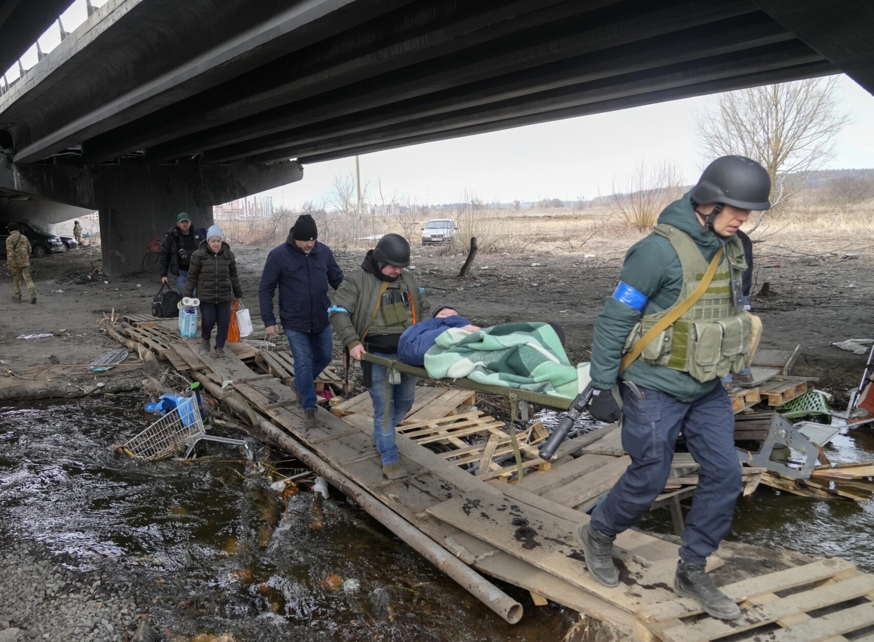 Ukrainians soldiers pass an improvised path under a destroyed bridge as they evacuate an elderly resident in Irpin, northwest of Kyiv, Saturday, March 12, 2022. Kyiv northwest suburbs such as Irpin and Bucha have been enduring Russian shellfire and bombardments for over a week prompting residents to leave their home. (AP Photo/Efrem Lukatsky)