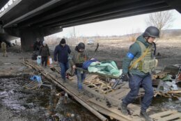 Ukrainians soldiers pass an improvised path under a destroyed bridge as they evacuate an elderly resident in Irpin, northwest of Kyiv, Saturday, March 12, 2022. Kyiv northwest suburbs such as Irpin and Bucha have been enduring Russian shellfire and bombardments for over a week prompting residents to leave their home. (AP Photo/Efrem Lukatsky)