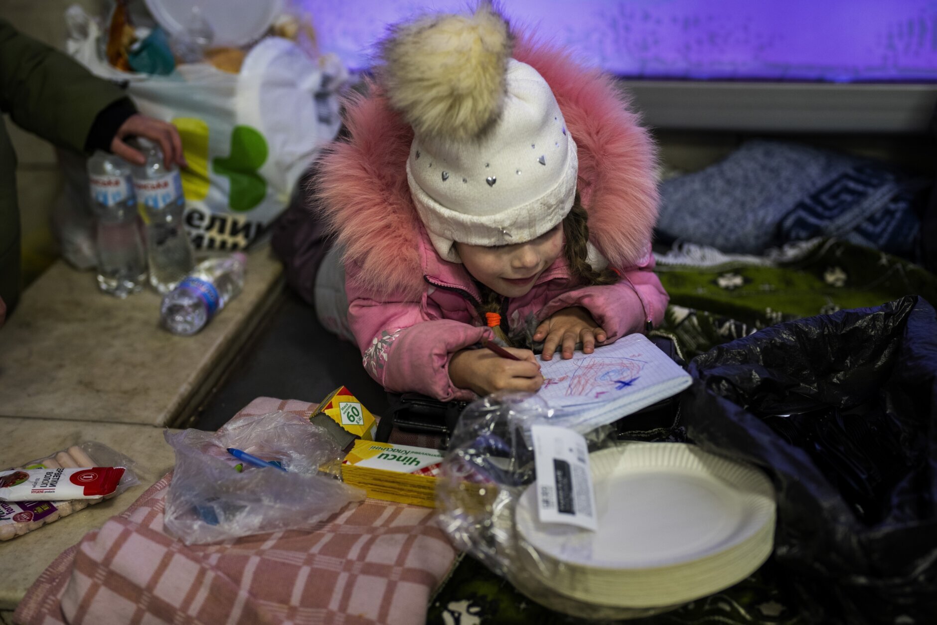 A girl paints on a note book next to her mother as they shelter in the Kyiv subway, using it as a bomb shelter, Ukraine, Saturday Feb. 26, 2022. (AP Photo/Emilio Morenatti)