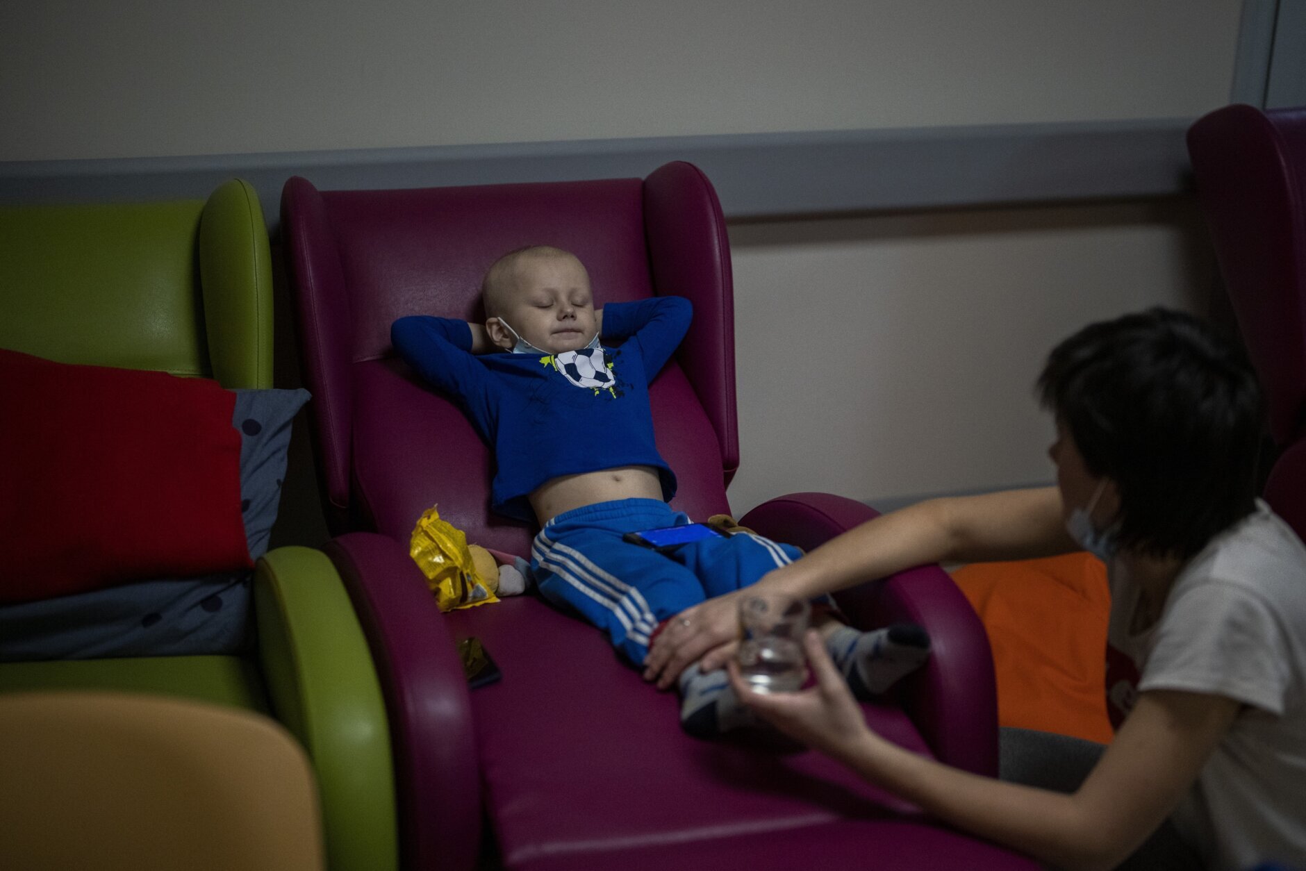 An oncology patient rests on a coach next to his mother, in a basement using it as a bomb shelter, while the sirens sound announcing new attacks, at the Okhmadet children's hospital in central Kyiv, Ukraine, Monday, Feb. 28, 2022. (AP Photo/Emilio Morenatti)