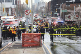 Law enforcement gather near the entrance to a subway stop in the Brooklyn borough of New York, Tuesday, April 12, 2022.  Multiple people were shot and injured Tuesday at a subway station in New York City during a morning rush hour attack that left wounded commuters bleeding on a train platform.. (AP Photo/Kevin Hagen).