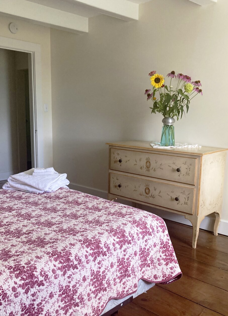 This image released by Aileen Weintraub shows a vintage dresser adorned with bouquet of flowers in a vase converted from an oversized novelty salt shaker in a bedroom at her home. Weintraub is a veteran of grappling with hand-me-down furnishings. Her recently published memoir, “Knocked Down,” details the months she spent on bedrest in a house filled with items her husband’s family owned for generations. (Aileen Weintraub via AP)