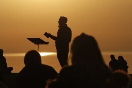 FILE - Park Community Church Associate Pastor Trevor Lovell is silhouetted against the sky as he leads an Easter sunrise service while parishioners listen on Sunday, April 4, 2021, at North Avenue Beach in Chicago. In a convergence that happens only rarely, Judaism’s Passover, Christianity’s Easter and Islam’s holy month of Ramadan are interlapping in April with holy days for Buddhists, Baha’is, Sikhs, Jains and Hindus, offering different faith groups a chance to share meals and rituals in a range of interfaith events. (AP Photo/Shafkat Anowar, File)