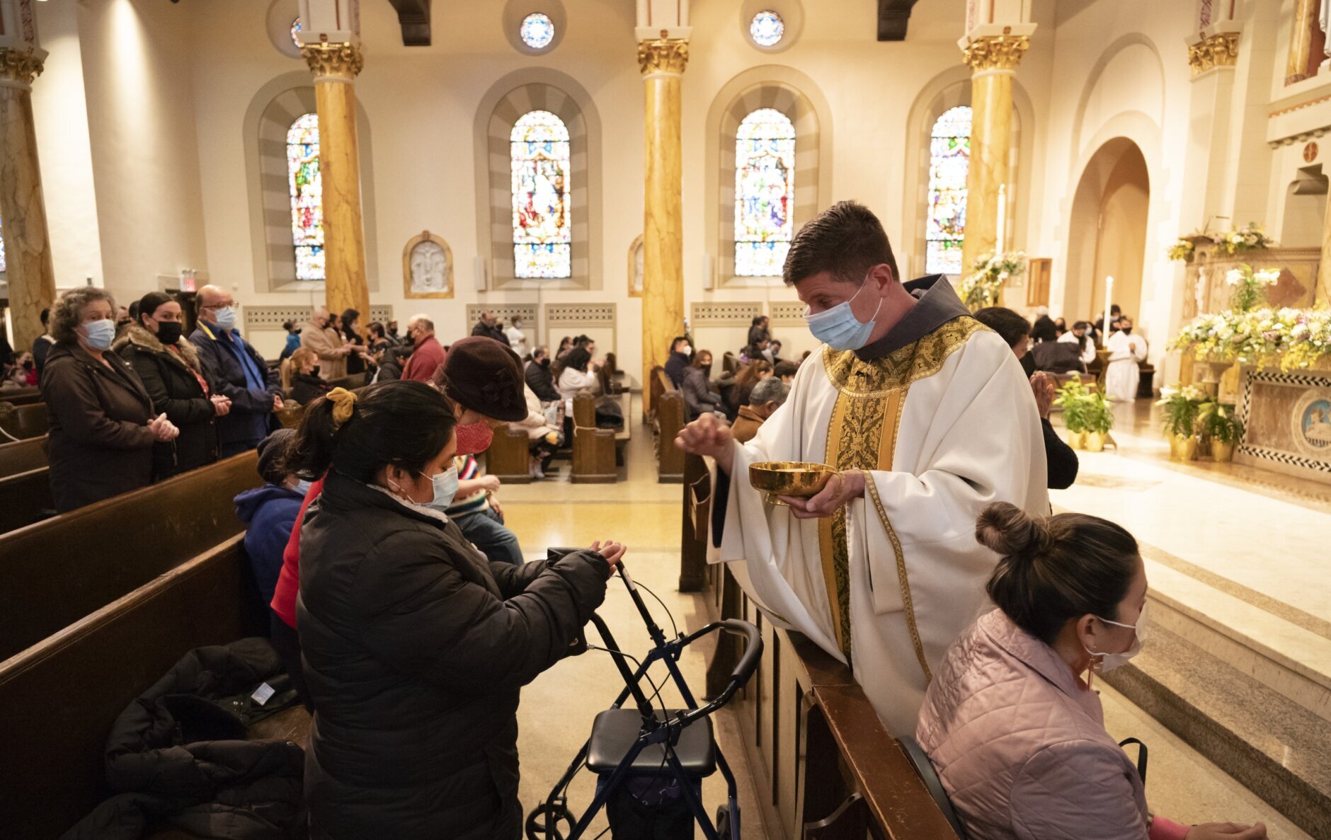 FILE - Rev. Russels Governale serves communion during a Spanish-language Easter service at St. Bartholomew Roman Catholic Church, which lost 80 of its members to COVID-19, Sunday, April 4, 2021, in New York. This year, in a rare convergence, Judaism’s Passover, Christianity’s Easter and Islam’s holy month of Ramadan are interlapping in April with holy days for Buddhists, Baha’is, Sikhs, Jains and Hindus, offering different faith groups a chance to share meals and rituals in a range of interfaith events. (AP Photo/Mark Lennihan)