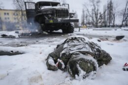 The body of a serviceman is coated in snow next to a destroyed Russian military multiple rocket launcher vehicle on the outskirts of Kharkiv, Ukraine, Friday, Feb. 25, 2022. (AP Photo/Vadim Ghirda)
