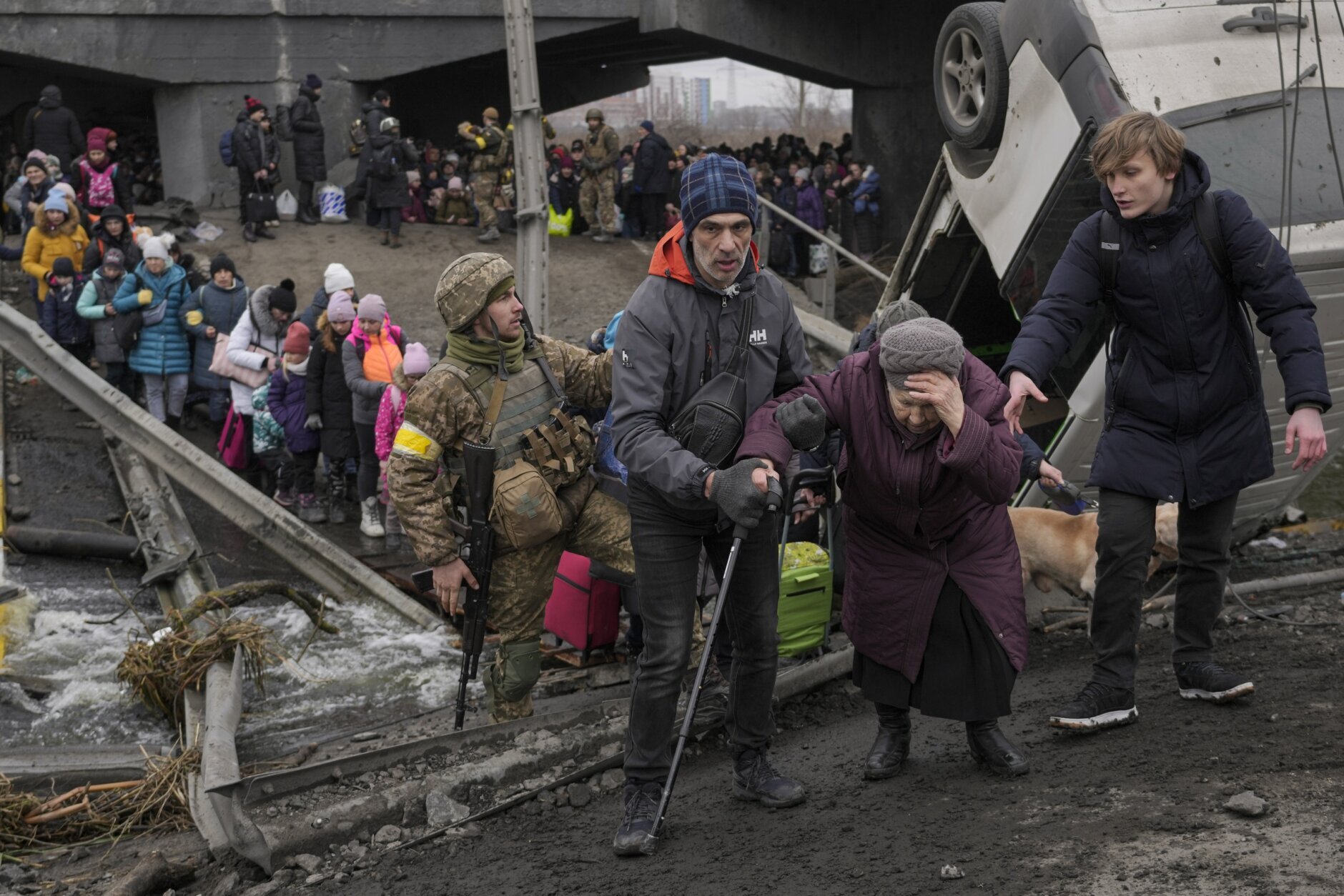 An elderly lady gets assisted while crossing the Irpin river, under a bridge that was destroyed, as civilians flee the town of Irpin, Ukraine, Saturday, March 5, 2022. (AP Photo/Vadim Ghirda)