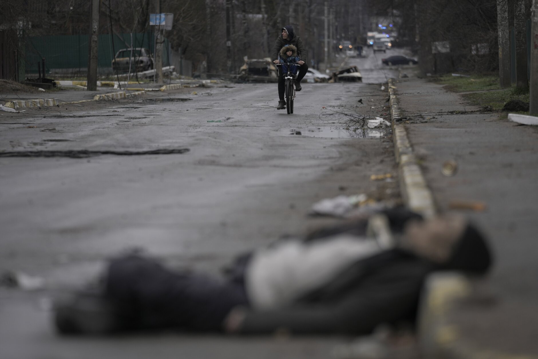 A man and child ride on a bicycle as bodies of civilians lie in the street in the formerly Russian-occupied Kyiv suburb of Bucha, Ukraine, Saturday, April 2, 2022. (AP Photo/Vadim Ghirda)