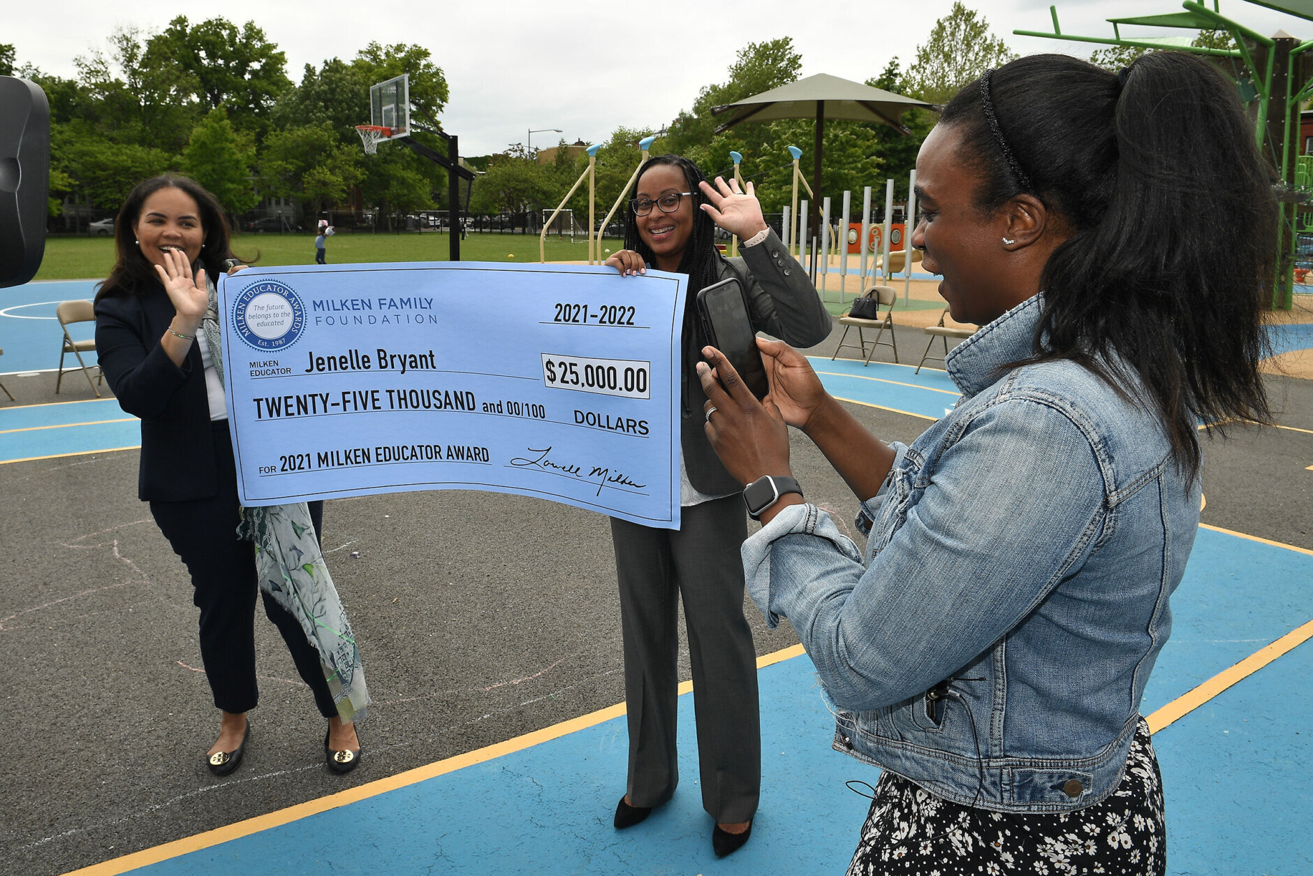 Jenelle Bryant FaceTimes her husband to tell him about her surprise Milken Educator Award. She points her phone at the huge check, held by Washington D.C. Superintendent of Education Dr. Christina Grant (left) and Dr. Shavonne Gibson, OSSE assistant superintendent, to show him that it bears her new last name (the two married recently). 
