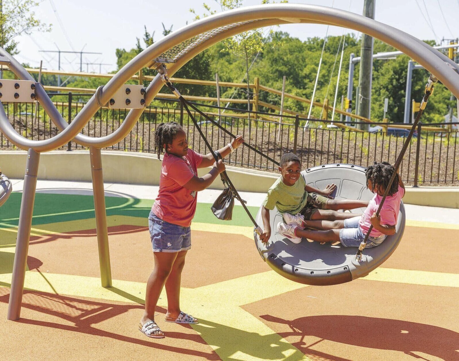 Brielle Mills (left), 9, swings twins Leilani and Jelanie Turner, 5, at the Harbor Drive Wellness Park. 