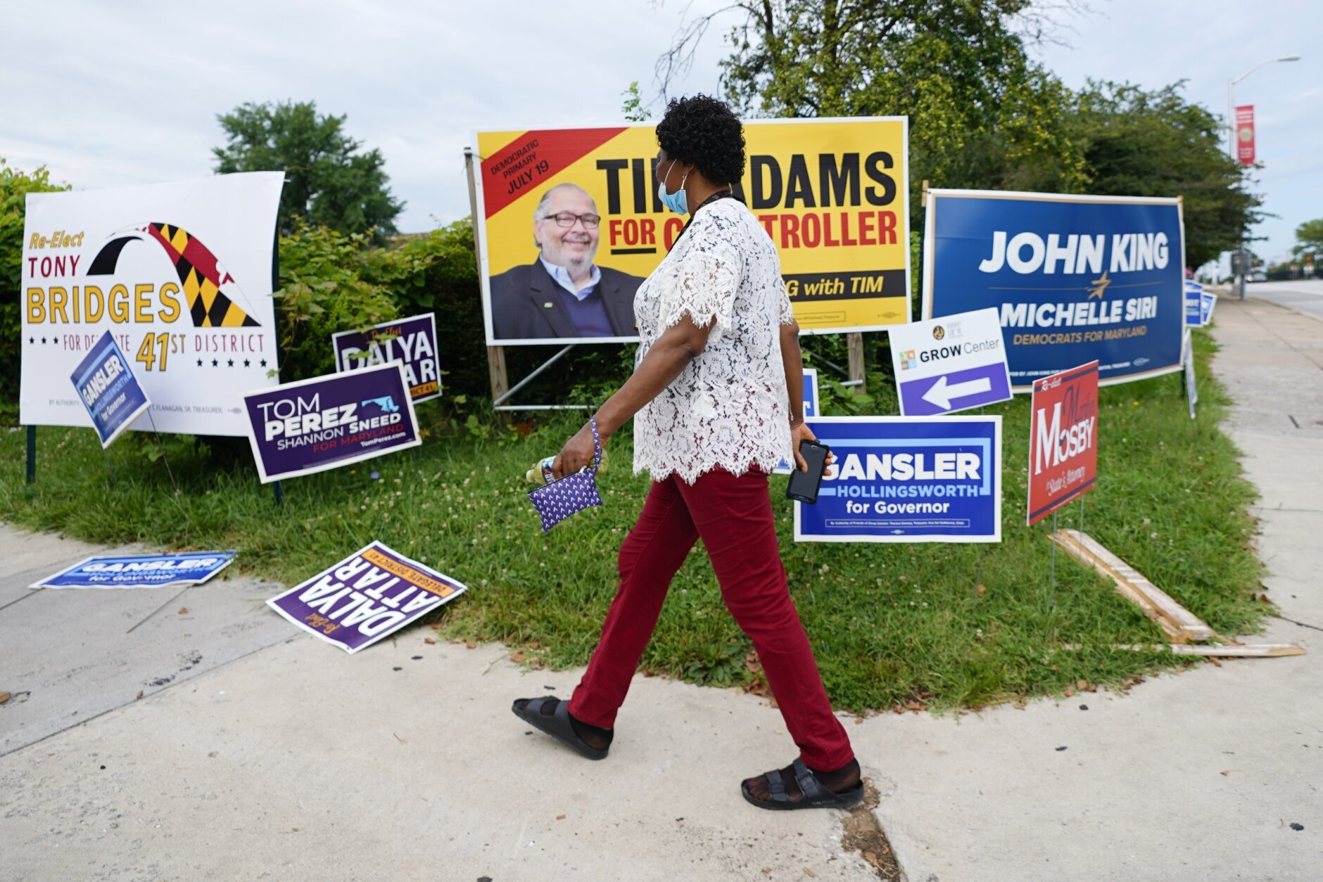 A woman walks in front of campaign signs during Maryland's primary election, Tuesday, July 19, 2022, in Baltimore. (AP Photo/Julio Cortez)