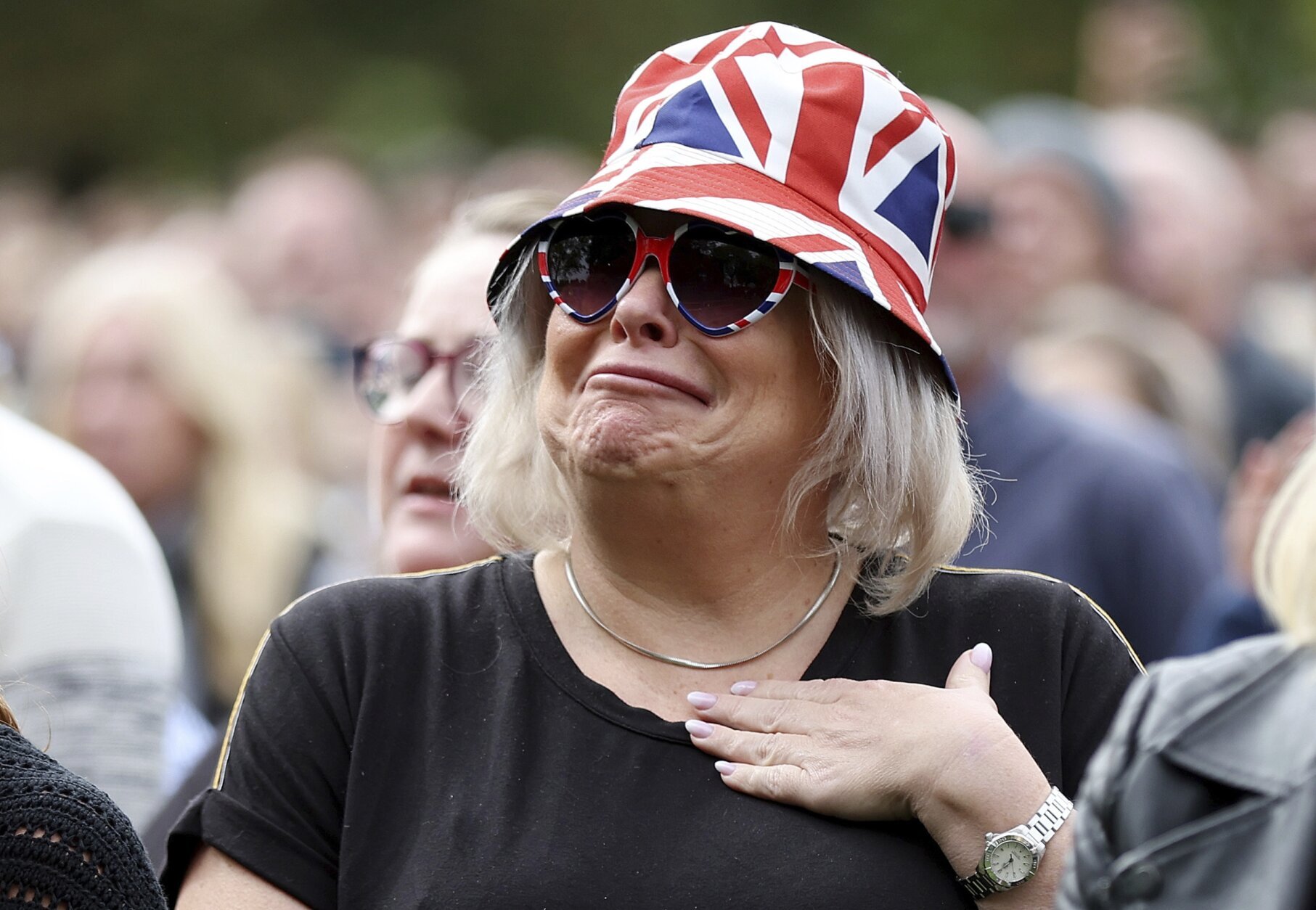 A woman reacts as she watches the Queen Elizabeth II funeral on a giant screen set near Windsor Castle, in Windsor, England, Monday, Sept. 19, 2022, before the committal service at St George's Chapel of Queen Elizabeth II. (Alex Pantling/Pool photo via AP)