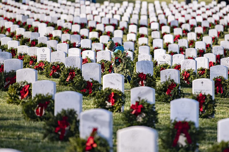 A boy sits in a row of headstones after volunteers layed wreaths on headstones at Arlington National Cemetery on Dec. 17, 2022.