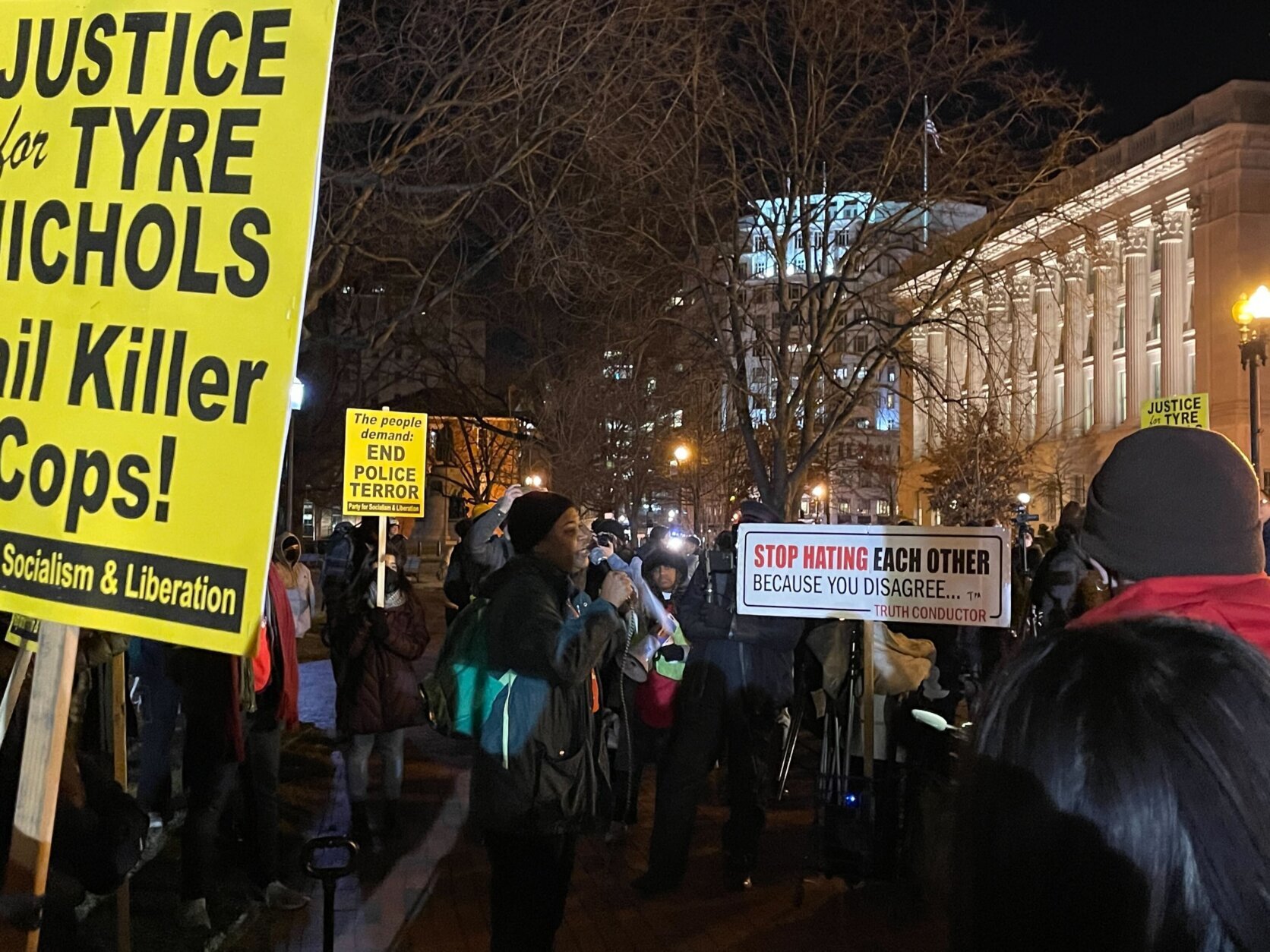 A Party for Socialism and Liberation protester giving a speech in downtown D.C. surrounded by people holding signs that read "Stop Hating Each Other Because You Disagree …" and "The people demand: End Police Terror."