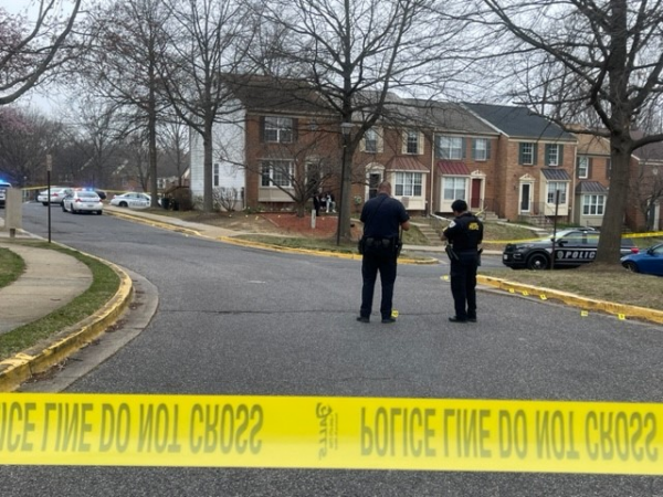 Photo of two police officers standing in the middle of a suburban road with bright yellow crime tape in the foreground.