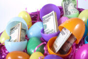 An Easter basket full of eggs with paper money on white background. Focus on the $100 bill in the center.
