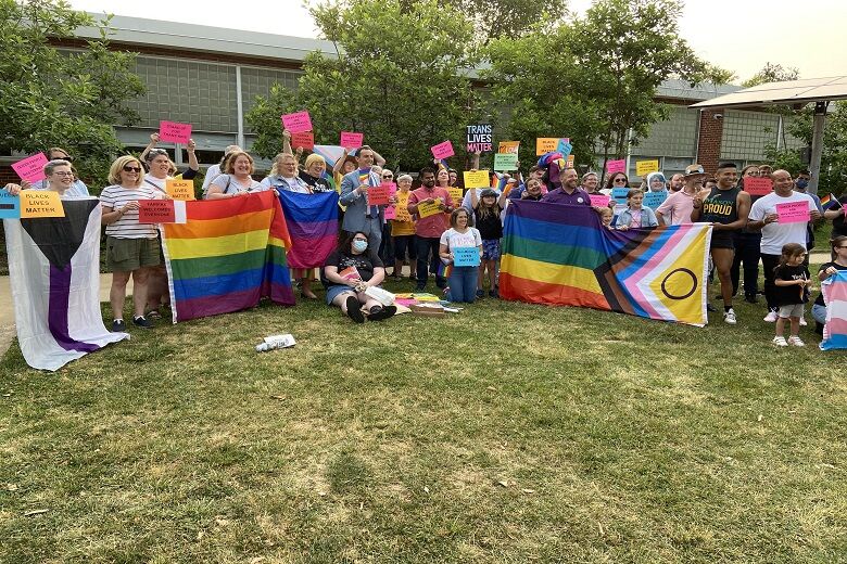 People at a Pride rally pose with rainbow flags
