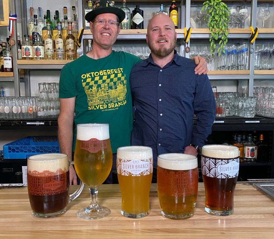 Christian Layke and Brett Robison from Silver Branch Brewing posing with a variety of beer glasses in the foreground.
