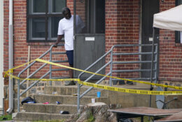 A person looks out the front door of a home as police tape surrounds the area of a mass shooting incident in the Southern District of Baltimore, Sunday, July 2, 2023. Police say a number of people were killed and dozens were wounded in a mass shooting that took place during a block party just after midnight. (AP Photo/Julio Cortez)