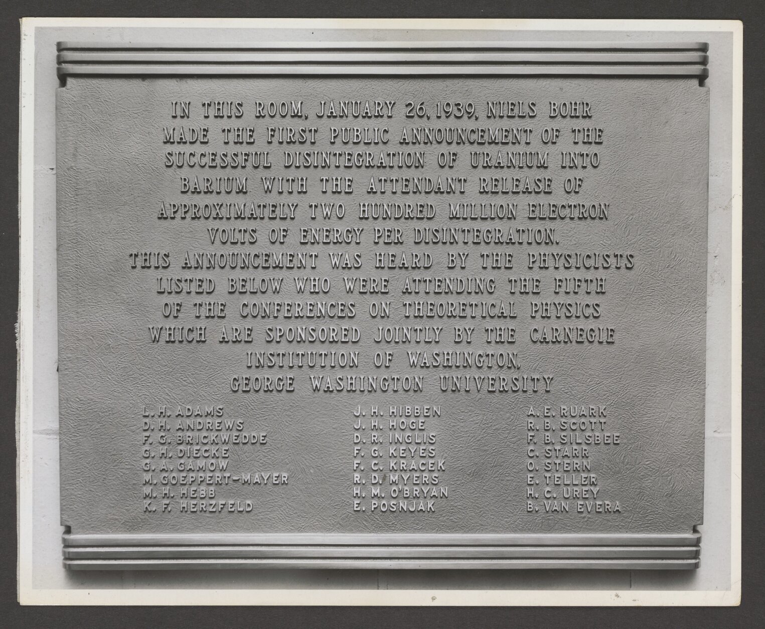 A black and white photograph of the Theoretical Physics Conference plaque, it contains the text "In this room, January 26, 1939, Niels Bohr made the first public announcement of the successful disintegration of uranium into barium with the attendant release of approximately two hundred million electron volts of energy per disintegration. (Courtesy of George Washington University)