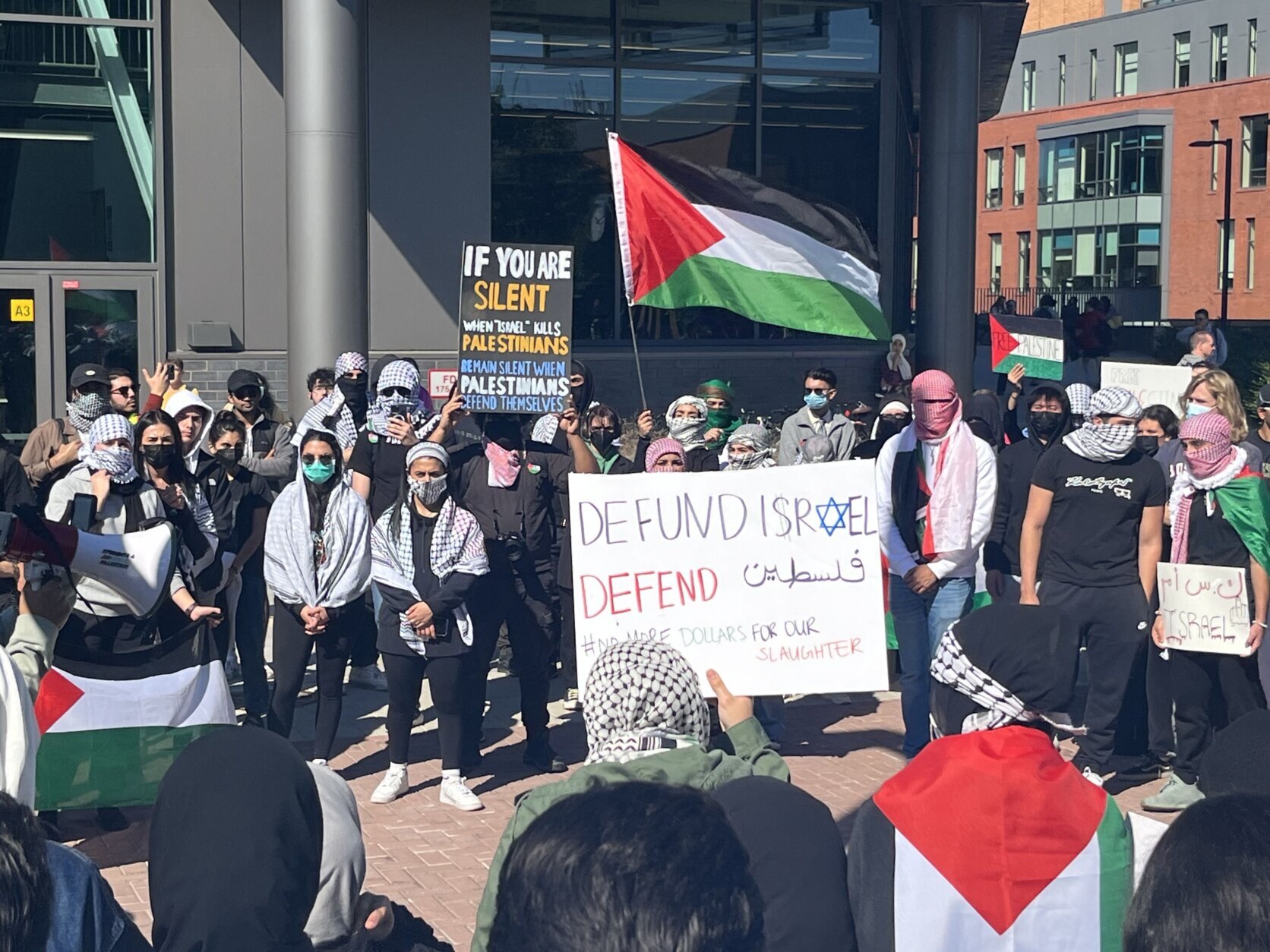 A crowd of students with signs and a Palestinian flag.