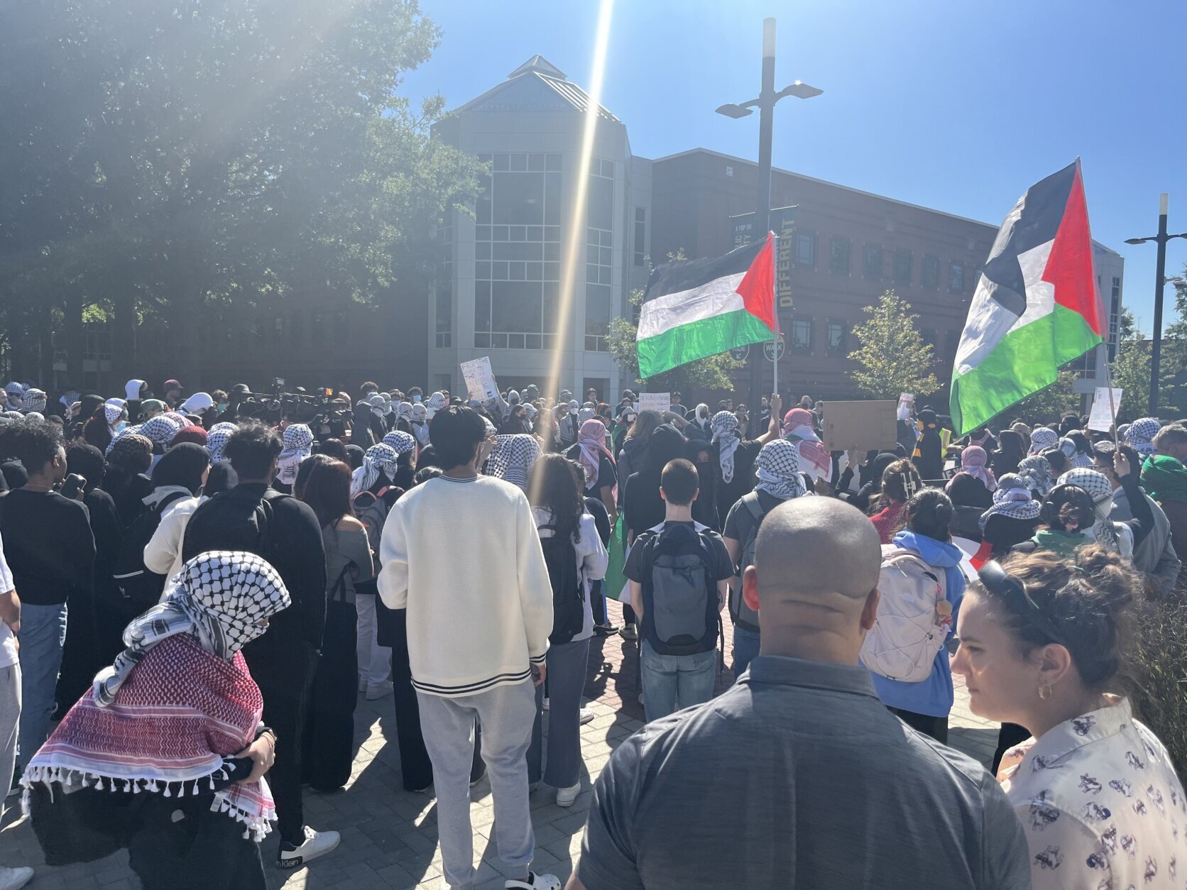 A crowd of students with Palestinian flags and a cross.