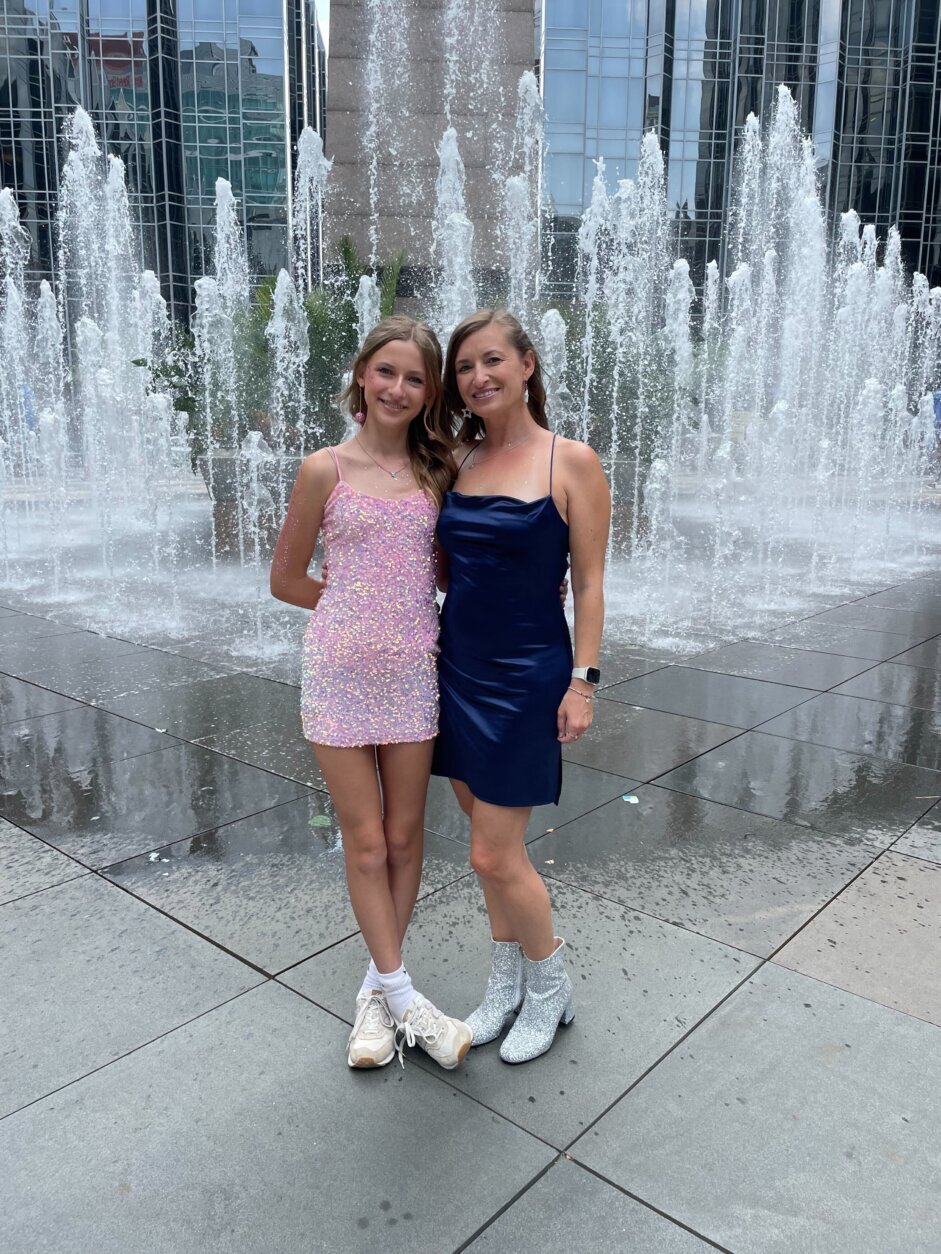 A mother and daughter stand in front of a fountain dressed in sequins and satin.