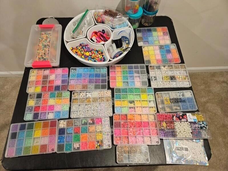 A table full of trays that hold beads and other bracelet making supplies