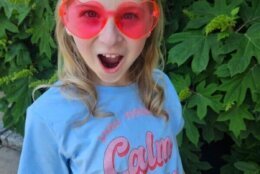 A young girl wears heart shaped glasses and a shirt that says "You Need to Calm Down."