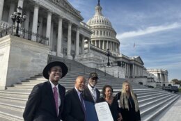 Sergeant Arthur Lee Martin stands at the steps of the U.S. Capitol Building in Washington, D.C. wearing a hat, just behind by four congressional leaders and staff members of color. Congressman Glenn Ivey stands in front of him holding a blue folder with a Congressional Citation inside.