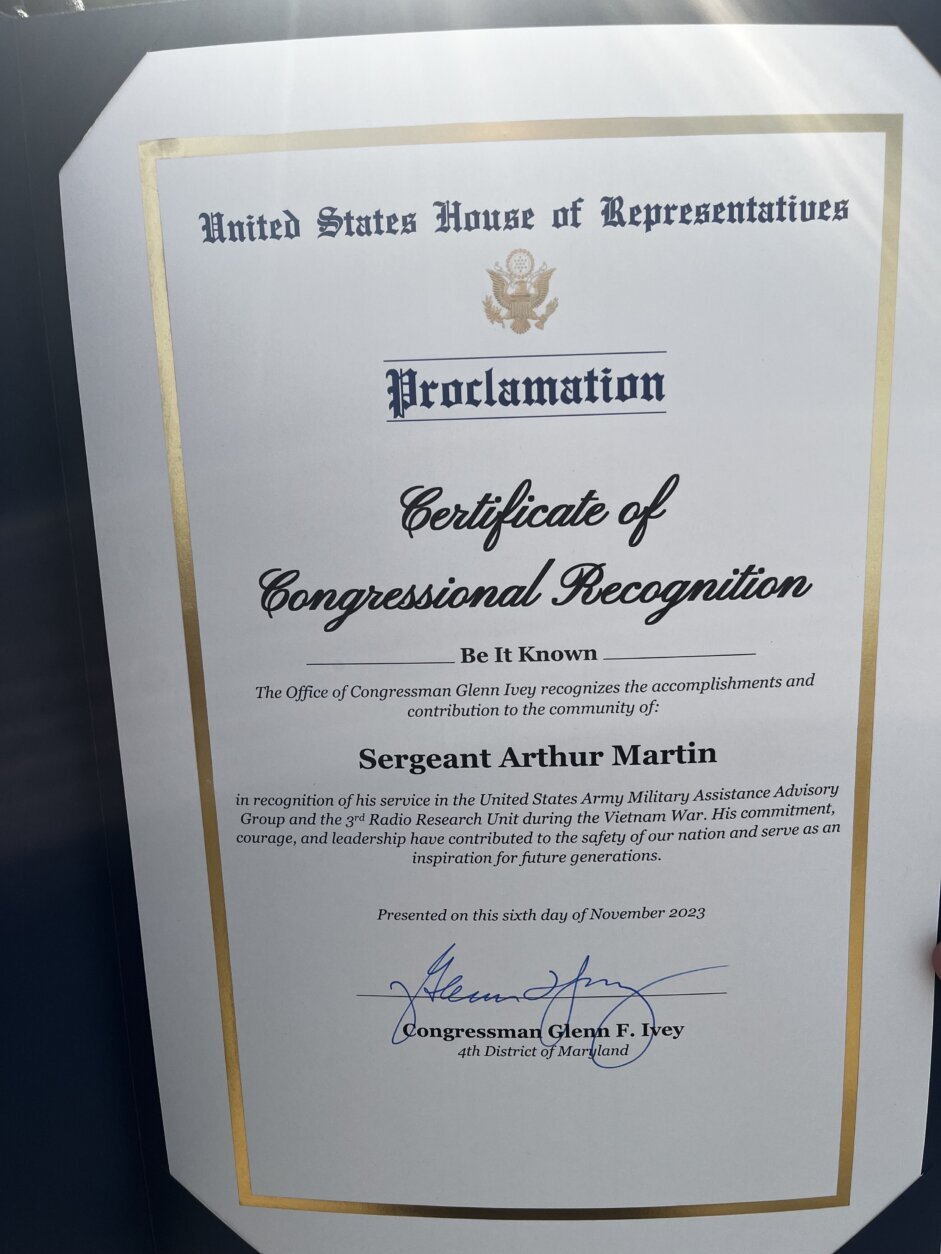 A proclamation from the U.S. House of Representatives sits inside a folder. Inside the paper's gold boarder, the proclamation reads: "Certificate of Congressional Recognition. Be it Known The office of Congressman Glenn Ivey recognizes the accomplishments and contribution to the community of: Sergeant Arthur Martin in recognition of his service in the United States Army Military Assistance Advisory Group and the 3rd Radio Research Unit during the Vietnam War. His commitment, courage, and leadership have contributed to the safety of our nation and serve as an inspiration for future generations. Presented on the sixth day of November 2023." The document is signed by Congressman Glenn F. Ivey, Representative of the 4th District of Maryland, in bold blue pen.