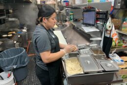 a woman in a restaurant's kitchen rolls up dough for pupusas