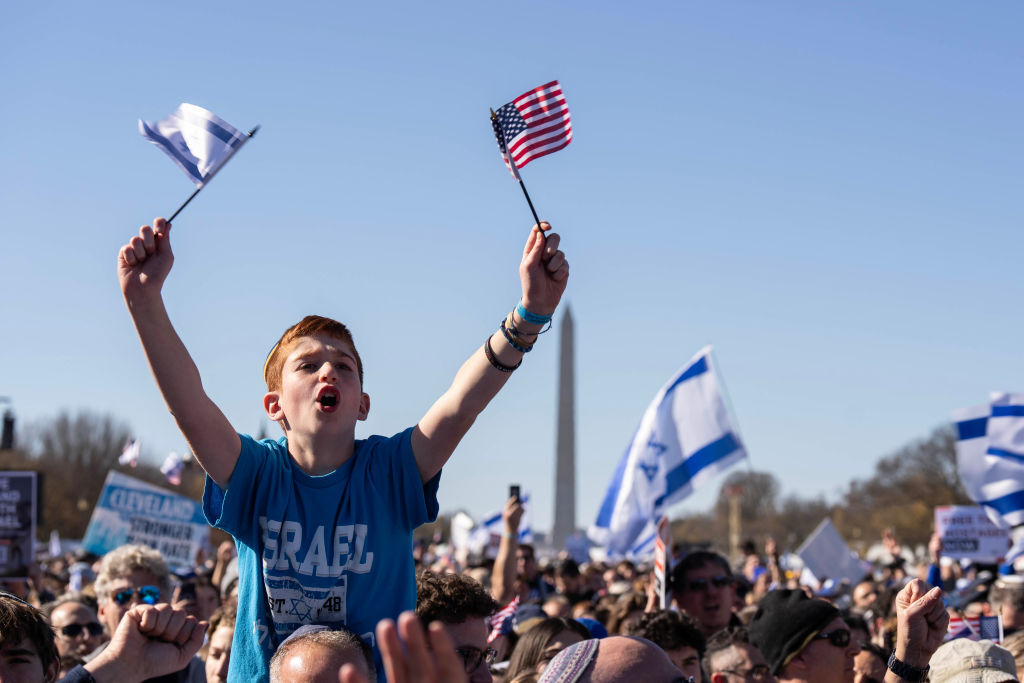hoisted on someone's shoulders above the crowd, a boy holds an American flag in one hand and Israel's in the other