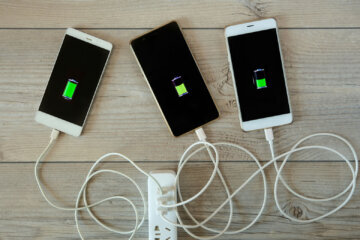 Smartphones are charged from the charger and lie side by side on the table. Charger for phone with connected USB cables, wires with smartphones.