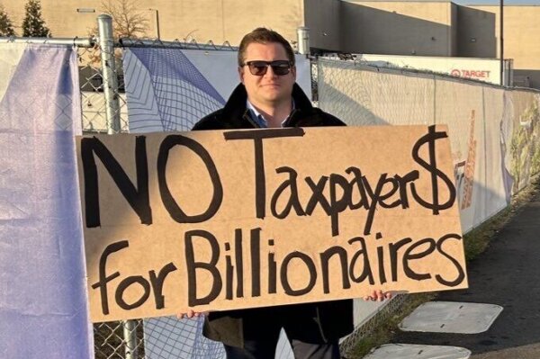 Man holding sign saying "No Taxpayer $ for Billionaires"