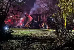 Wreckage of a house seen across a lawn, with plumes smoke billowing from it.
