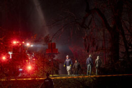 Fire and police officials walk around the scene of a house explosion