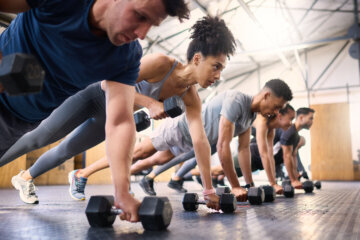 Strong, fitness and gym people with dumbbell teamwork training or exercise community, accountability and group. Sports diversity friends on floor in pushup muscle workout, power and wellness together