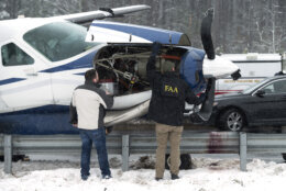 Federal Aviation Administration inspectors look at the engine of Southern Airways Express flight 246, which made an emergency landing on the Loudoun County Parkway, Friday afternoon, Jan. 19, 2024, in Dulles, Va., near Washington Dulles International Airport. There were seven people on board the single-engine Cessna 208 Caravan, according to the FAA, and no injuries were reported. (AP Photos/Clifford Owen)