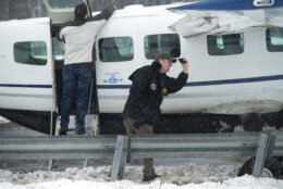 Federal Aviation Administration inspectors look at the engine of Southern Airways Express flight 246, which made an emergency landing on the Loudoun County Parkway, Friday afternoon, Jan. 19, 2024, in Dulles, Va., near Washington Dulles International Airport. There were seven people on board the single-engine Cessna 208 Caravan, according to  the FAA, and no injuries were reported. (AP Photos/Clifford Owen)
