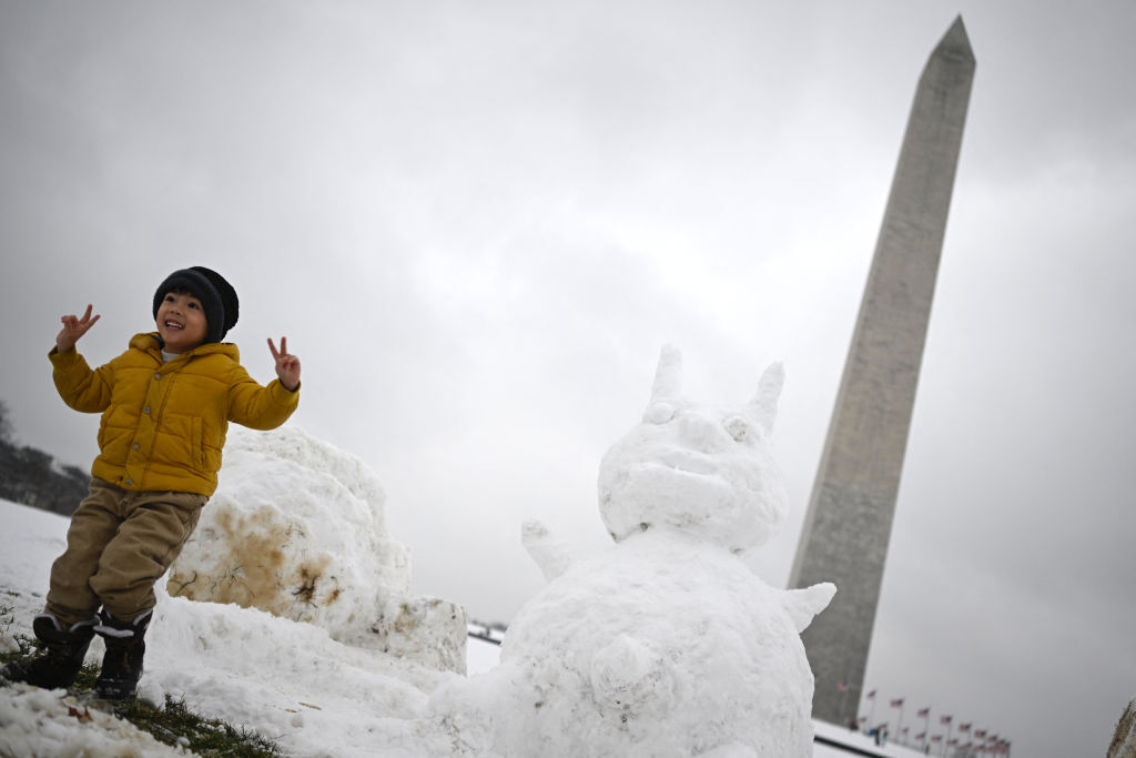A boy poses for a picture near a snowman at the Washington Monument, on the National Mall, in Washington, DC on January 16, 2024. The Washington DC metro region received between 2 and 4 inches of snow on January 15, 2024. (Photo by ANDREW CABALLERO-REYNOLDS / AFP) (Photo by ANDREW CABALLERO-REYNOLDS/AFP via Getty Images)