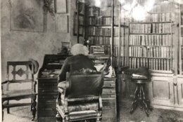 Black and white image of Frederick Douglass as he takes a seat at a desk in his library
