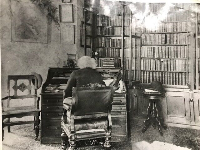 Black and white image of Frederick Douglass as he takes a seat at a desk in his library