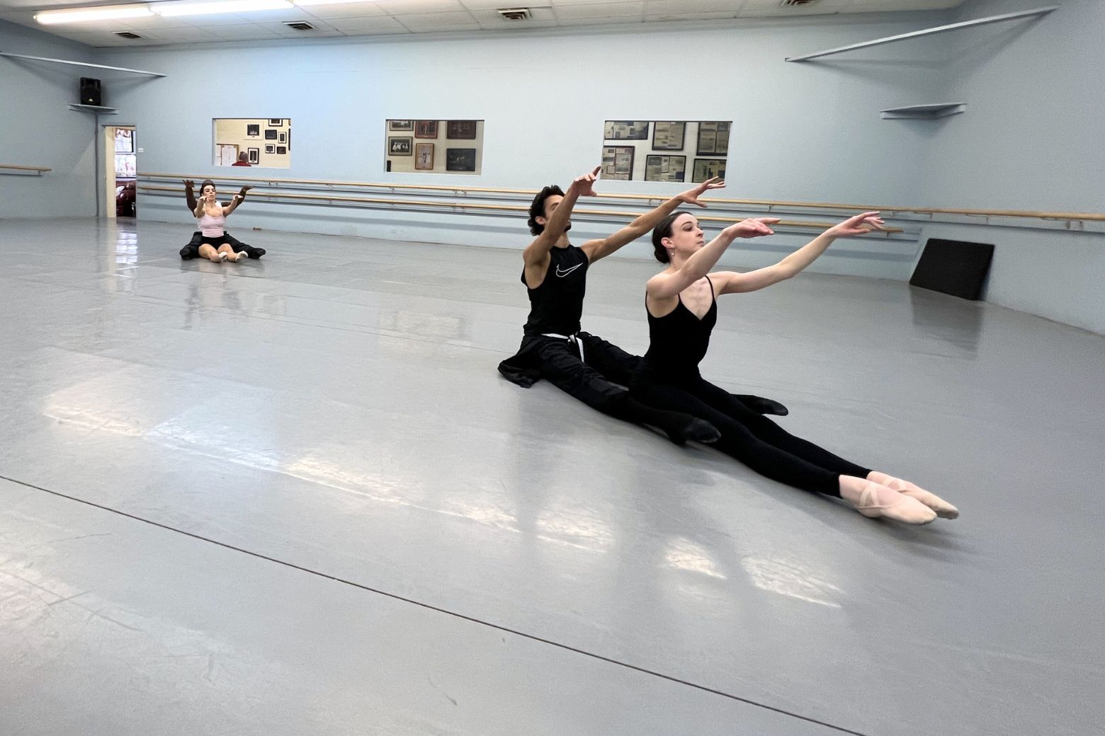 Dancers reach out while seated with their legs pointed toward the corner of the room.