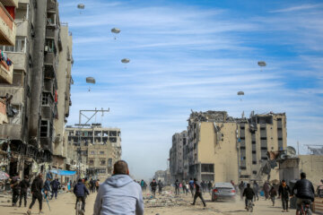 TOPSHOT - Palestinians run along a street as humanitarian aid is airdropped in Gaza City on March 1, 2024, amid the ongoing conflict between Israel and the Hamas militant group. For months, aid workers have warned of an increasingly desperate situation for Gazan civilians, and on February 26 an official from the UN humanitarian office OCHA said widespread starvation was "almost inevitable". (Photo by AFP) (Photo by -/AFP via Getty Images)
